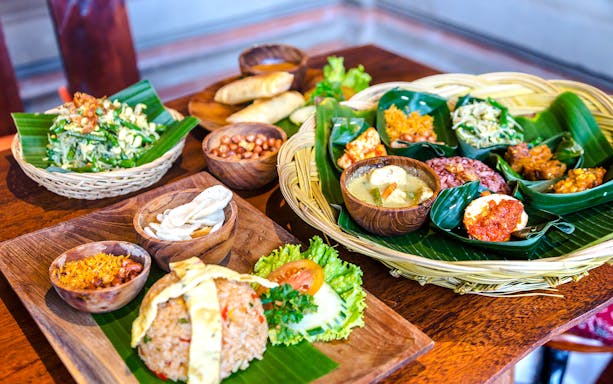 Balinese lunch spread with rice, vegetables, and traditional dishes on banana leaves.