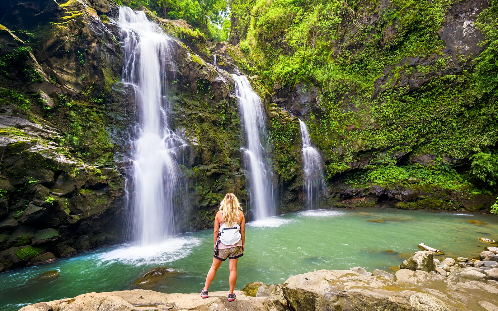 Waterfalls along the Road to Hana, Maui, with a person standing by the pool.
