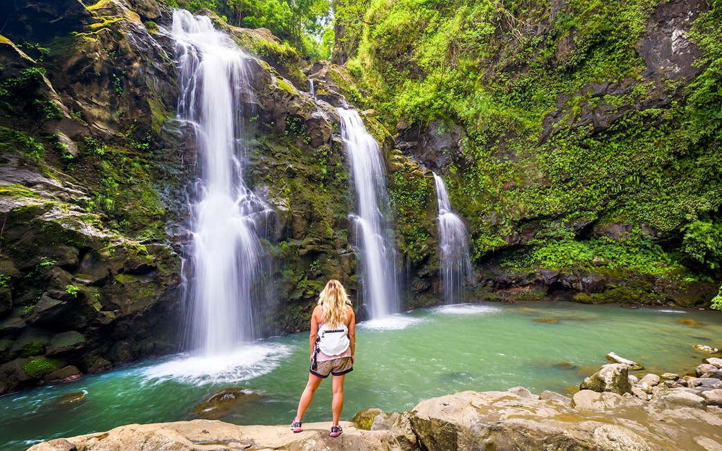 Waterfalls along the Road to Hana, Maui, with a person standing by the pool.