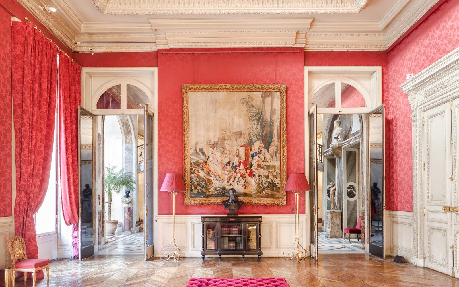 Jacquemart André Museum interior with ornate red walls, large tapestry, and classical sculptures.