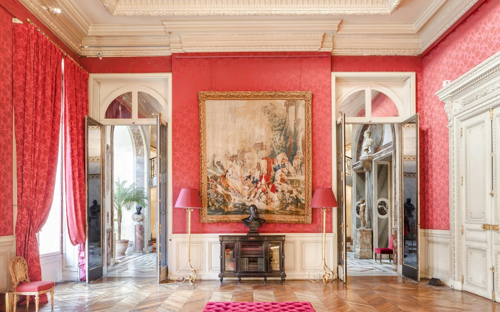 Jacquemart André Museum interior with ornate red walls, large tapestry, and classical sculptures.