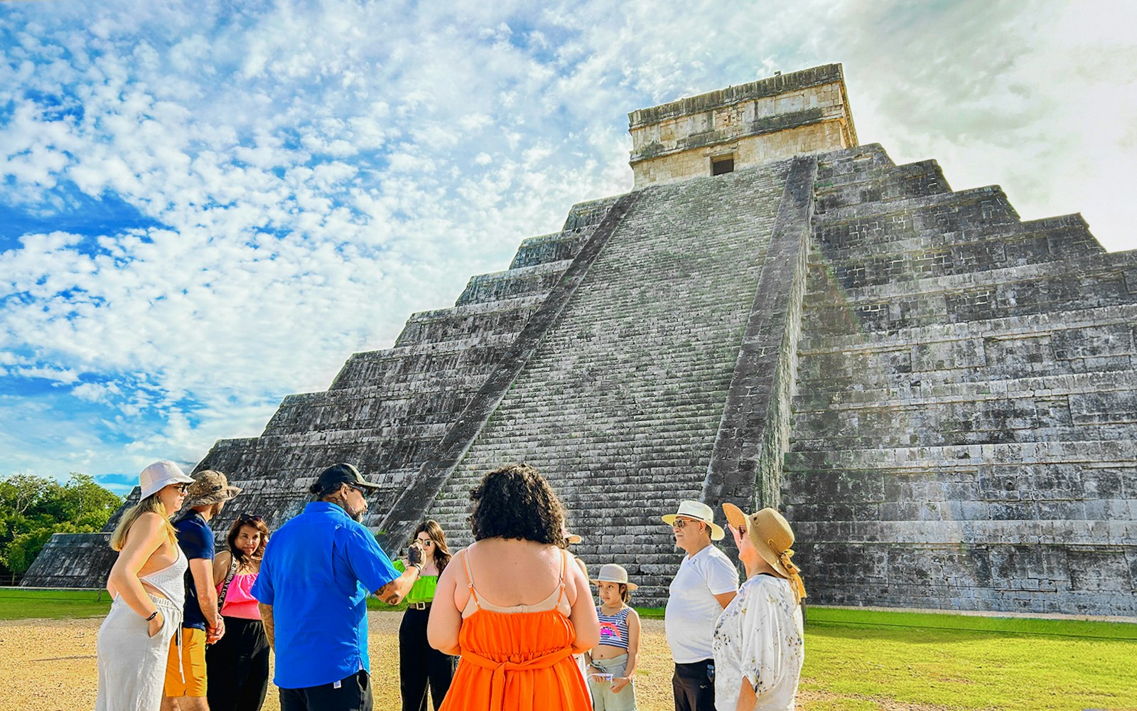Tour group at Chichen Itza pyramid, Mexico, with guide explaining site history.