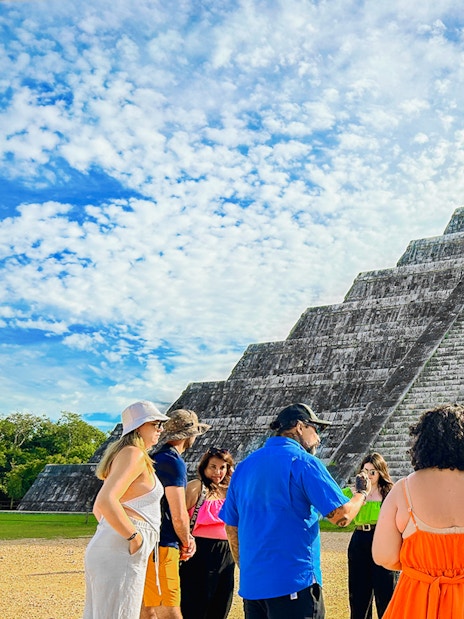 Tour group at Chichen Itza pyramid, Mexico, with guide explaining site history.