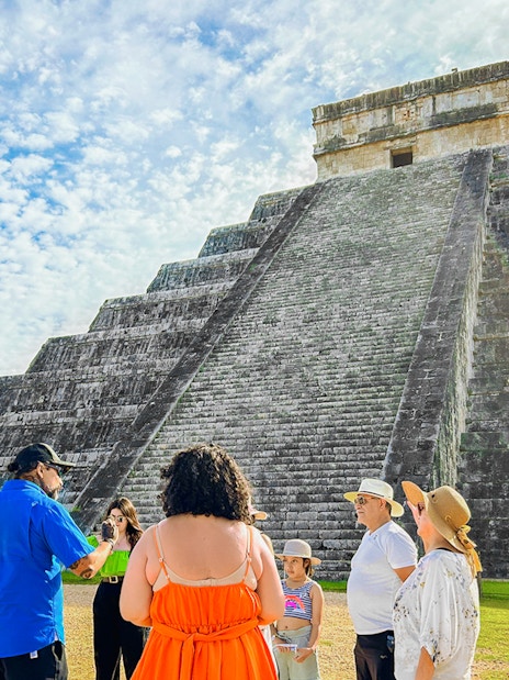 Tour group at Chichen Itza pyramid, Mexico, with guide explaining site history.