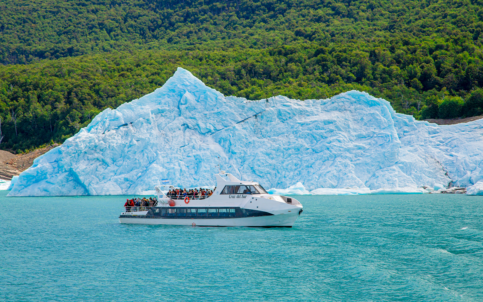 Tourists on a boat tour at Lago Argentino with a glacier backdrop in Los Glaciares National Park, Patagonia.