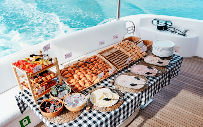 Breakfast buffet on luxury yacht cruise with pastries, fruits, and cold cuts.