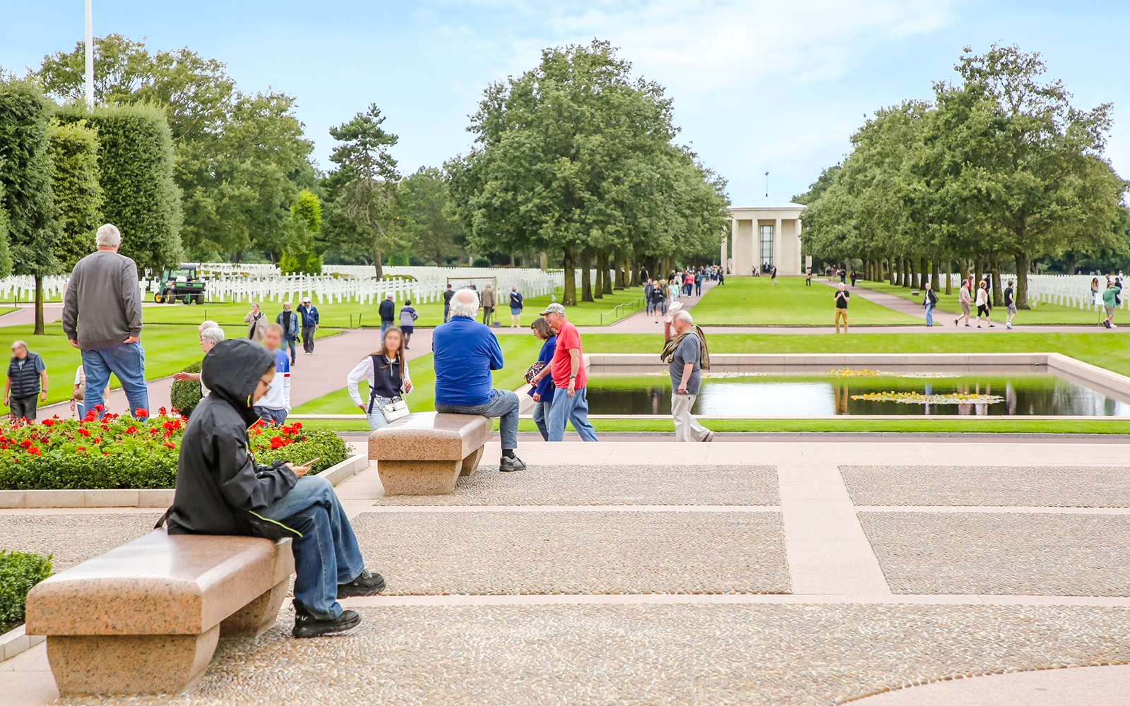 Visitors at Normandy American Cemetery and Memorial, Colleville-sur-Mer, France, with rows of crosses and memorial building.