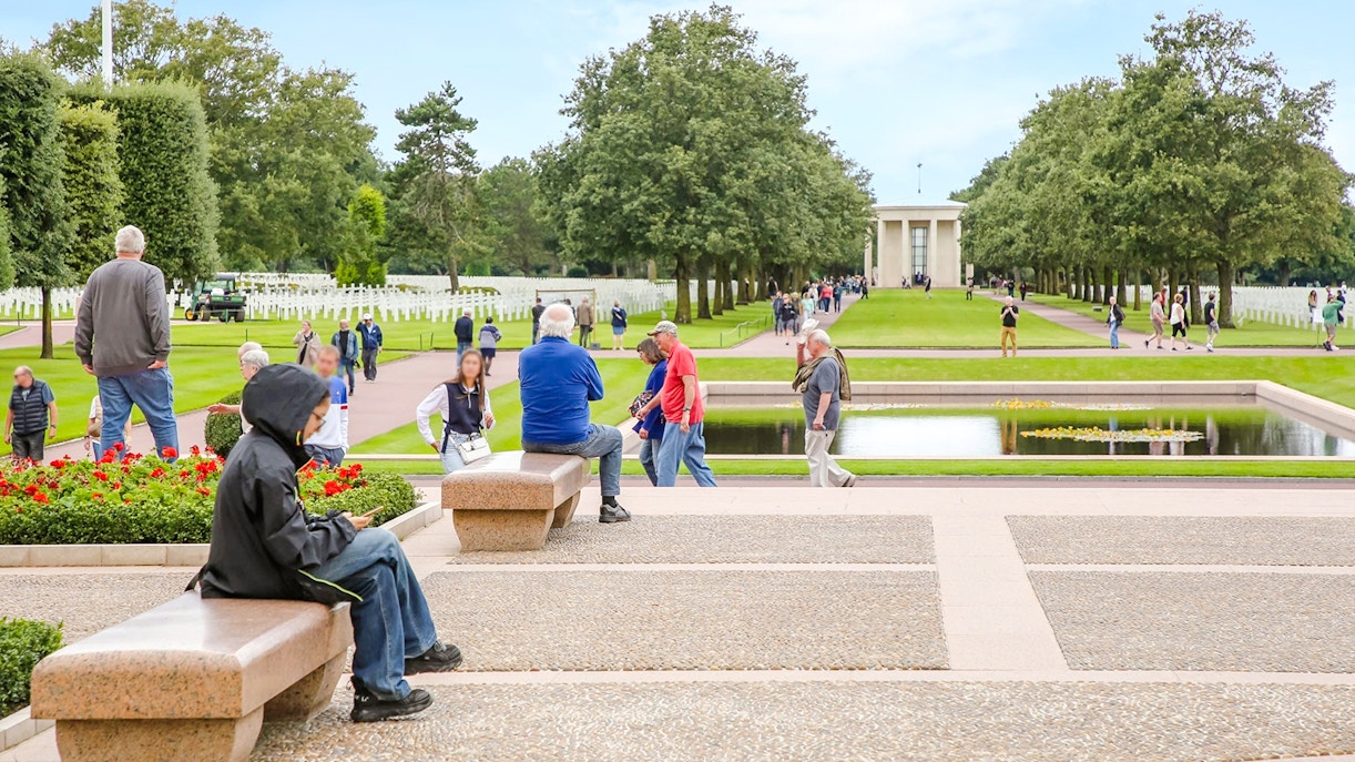 Visitors at Normandy American Cemetery and Memorial, Colleville-sur-Mer, France, with rows of crosses and memorial building.