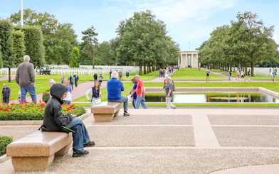 Visitors at Normandy American Cemetery and Memorial, Colleville-sur-Mer, France, with rows of crosses and memorial building.