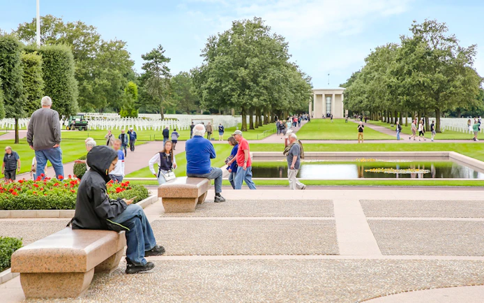 Visitors at Normandy American Cemetery and Memorial, Colleville-sur-Mer, France, with rows of crosses and memorial building.