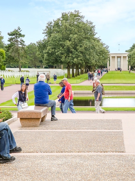 Visitors at Normandy American Cemetery and Memorial, Colleville-sur-Mer, France, with rows of crosses and memorial building.