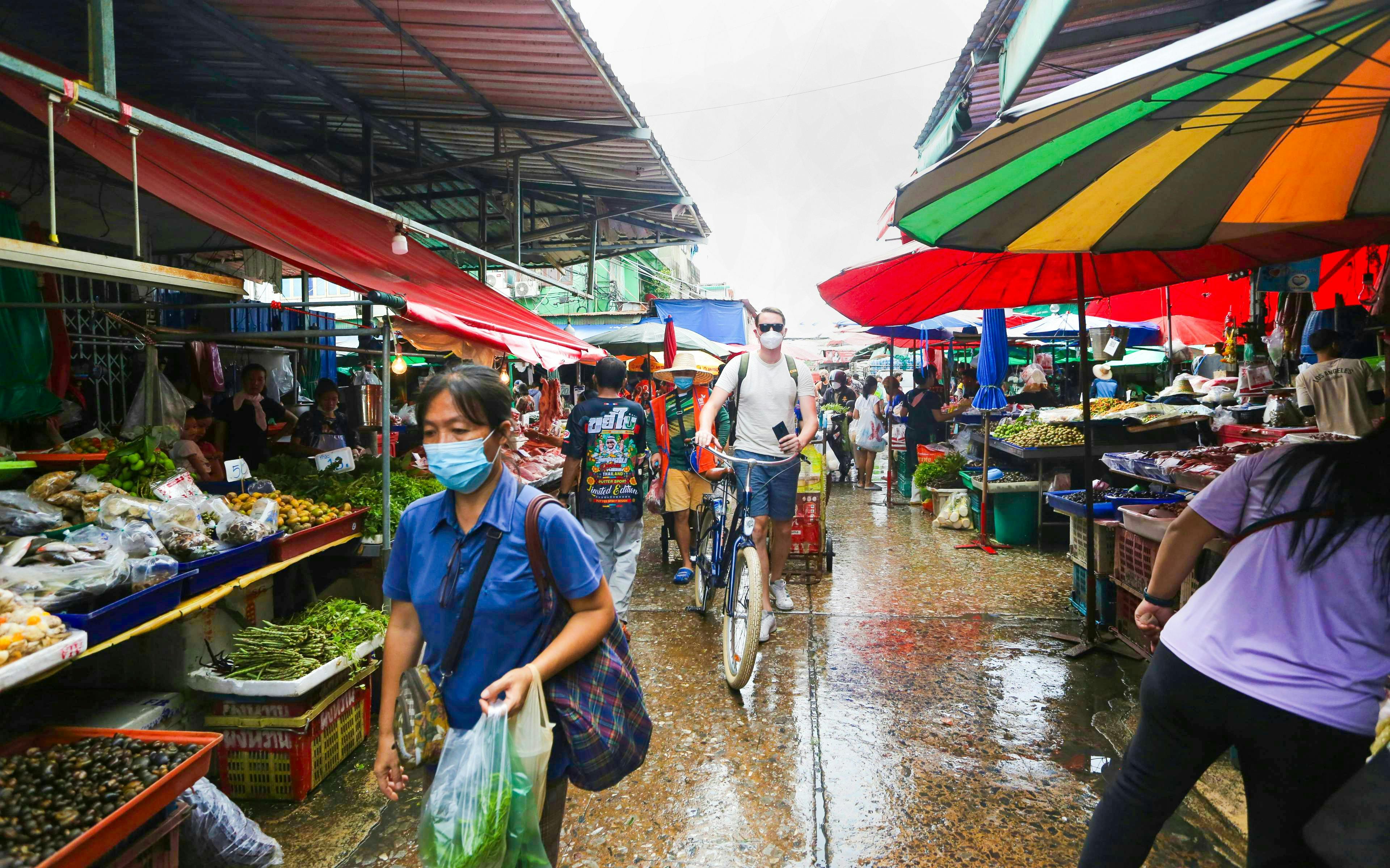 Cyclist navigating through a bustling Bangkok market with colorful stalls and local produce.