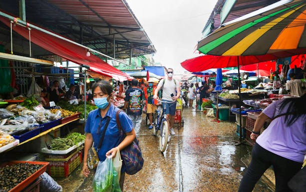 Cyclist navigating through a bustling Bangkok market with colorful stalls and local produce.