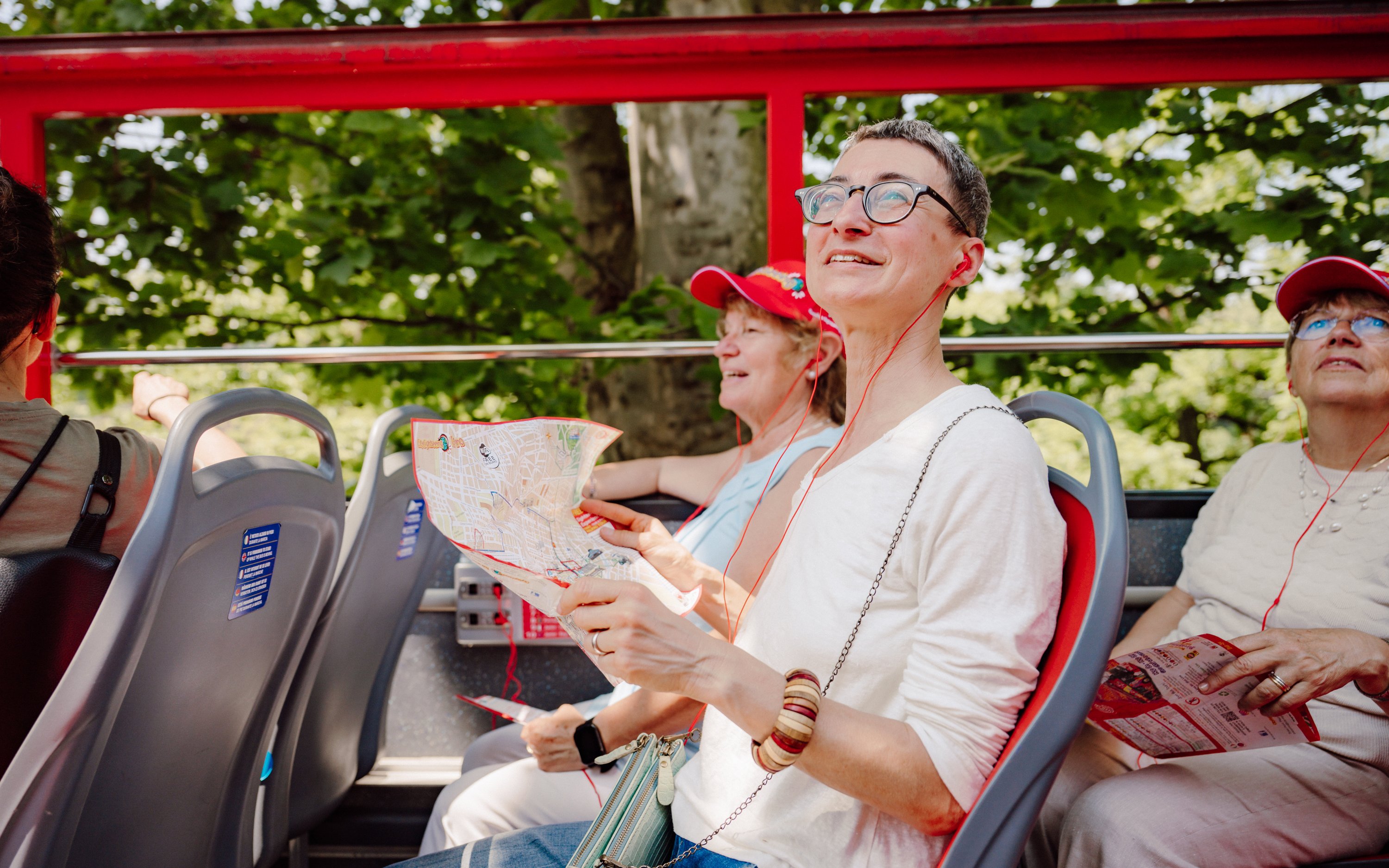 Tourists enjoying City Sightseeing Turin hop-on hop-off bus with maps and headphones.