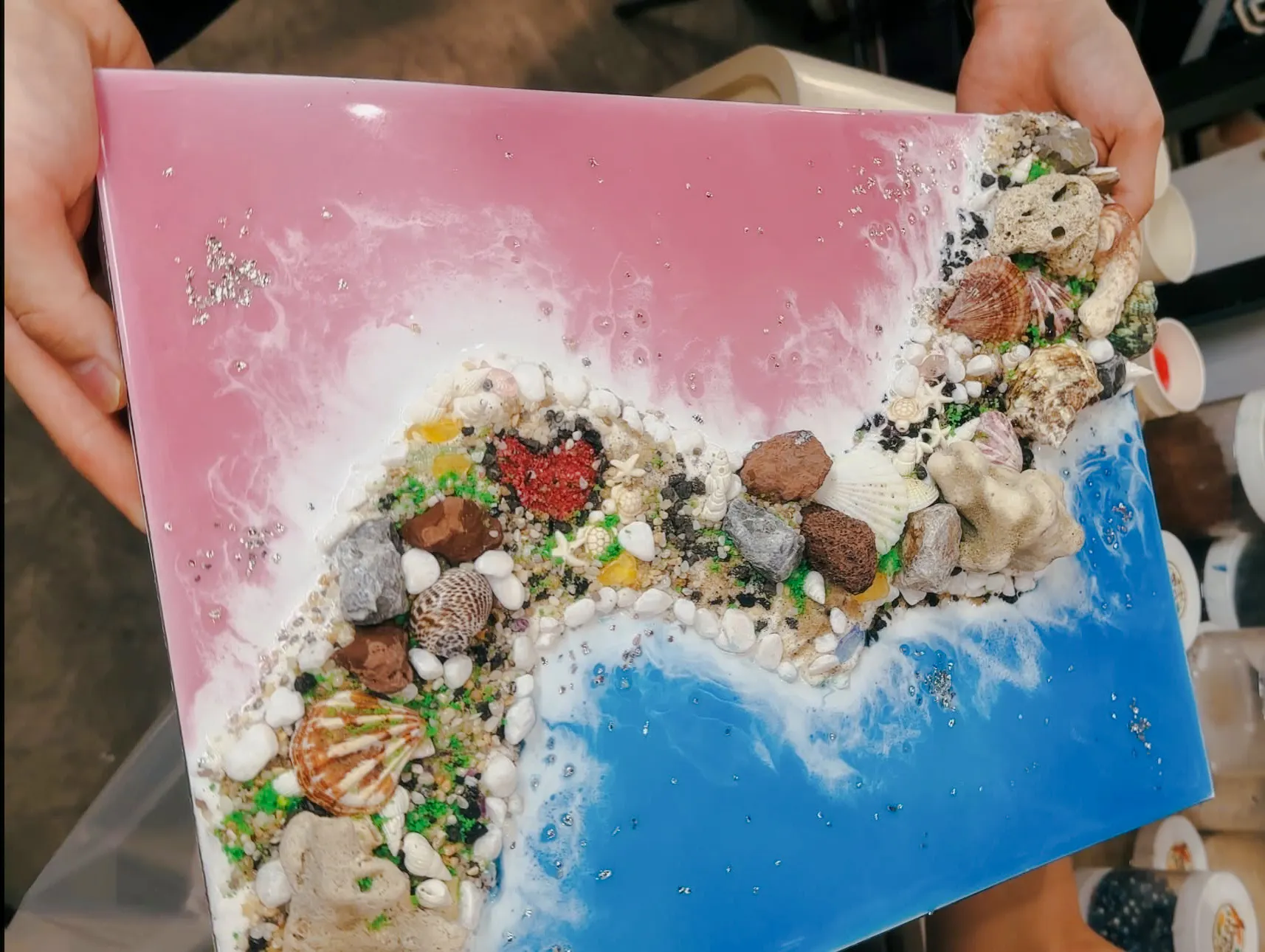 Artwork with seashells and stones on a pink and blue canvas, Hanoi art experience.