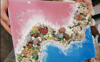 Artwork with seashells and stones on a pink and blue canvas, Hanoi art experience.
