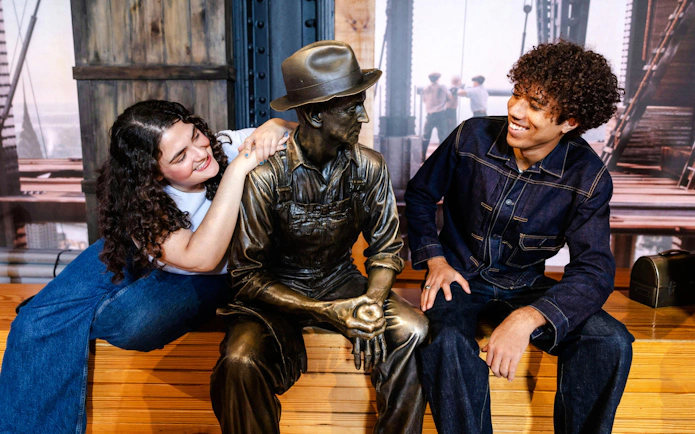 Visitors interacting with a worker statue at the Empire State Building exhibit.
