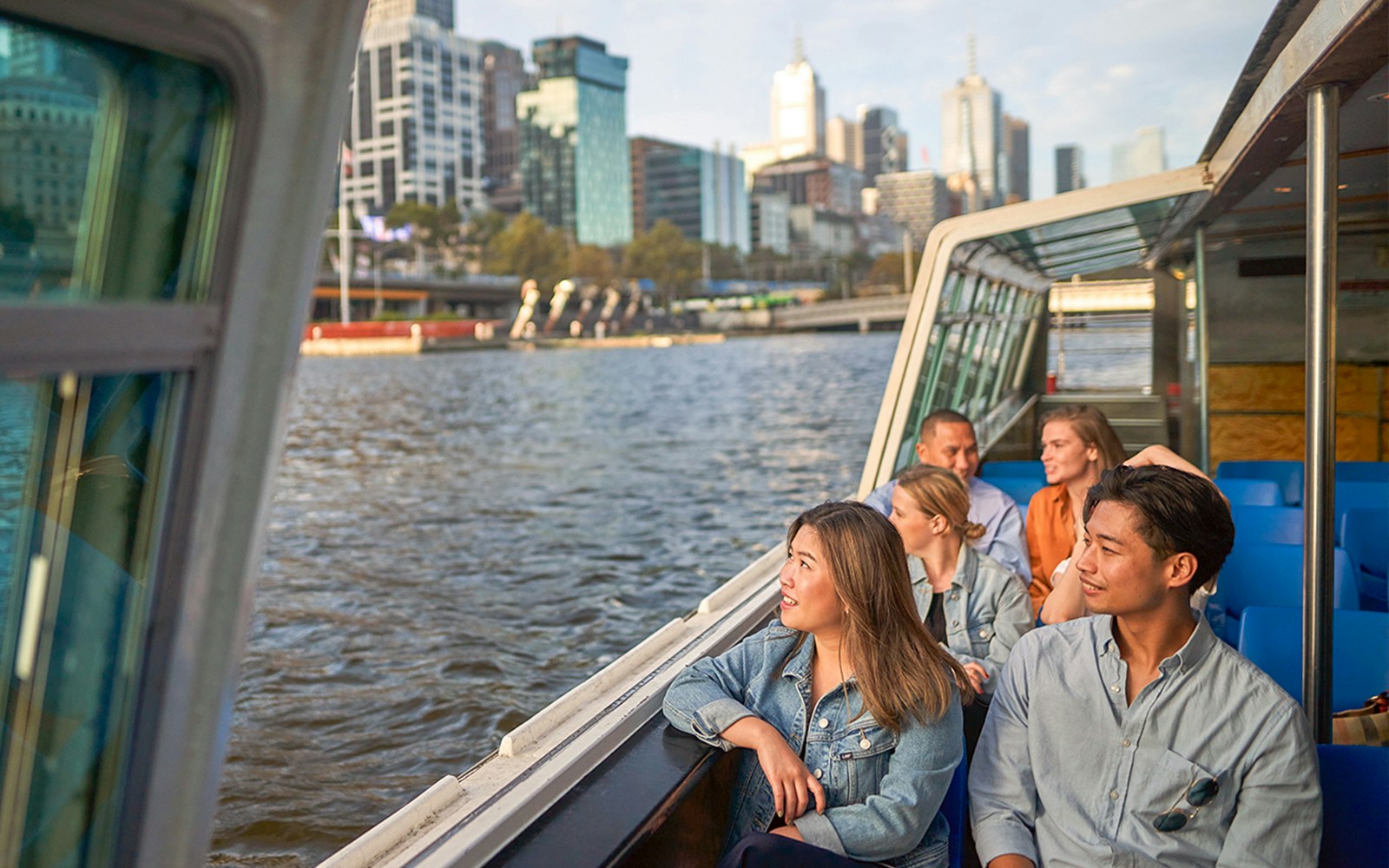 Melbourne River Cruise guests enjoying Yarra River views with city skyline in the background.