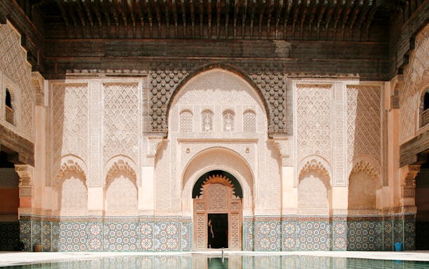 Ben Youssef Madrasa courtyard with intricate carvings and mosaic tiles in Marrakesh, Morocco.