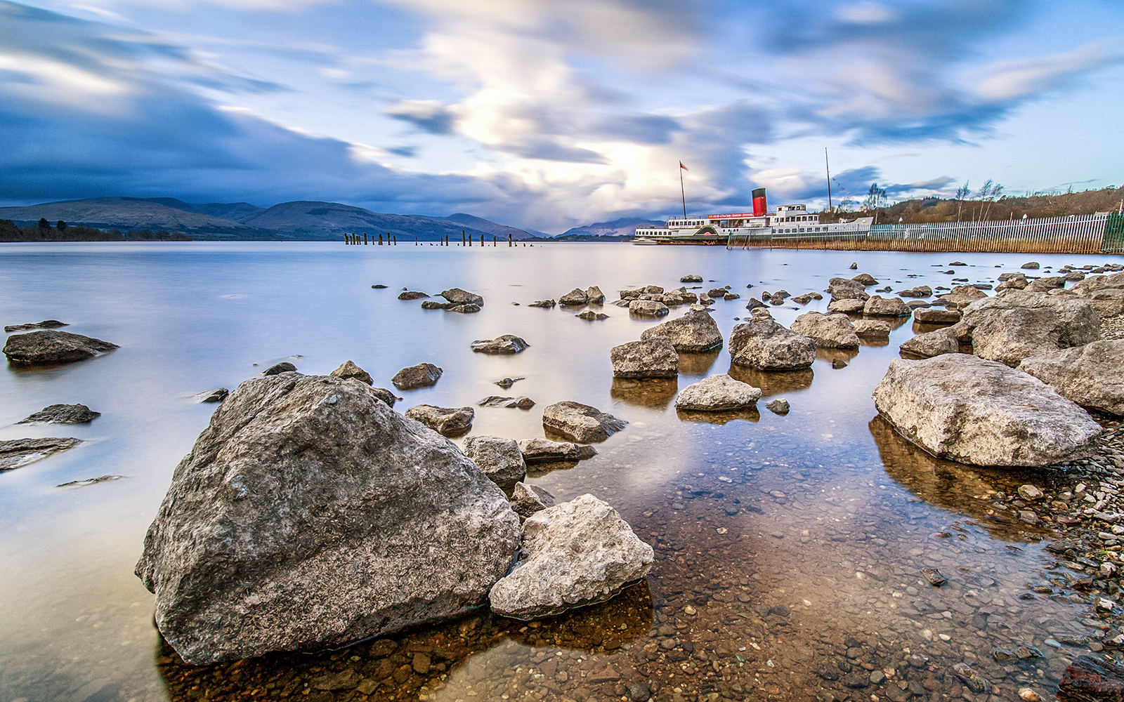 Steamboat on Loch Lomond Lake with rocky shoreline and distant hills.