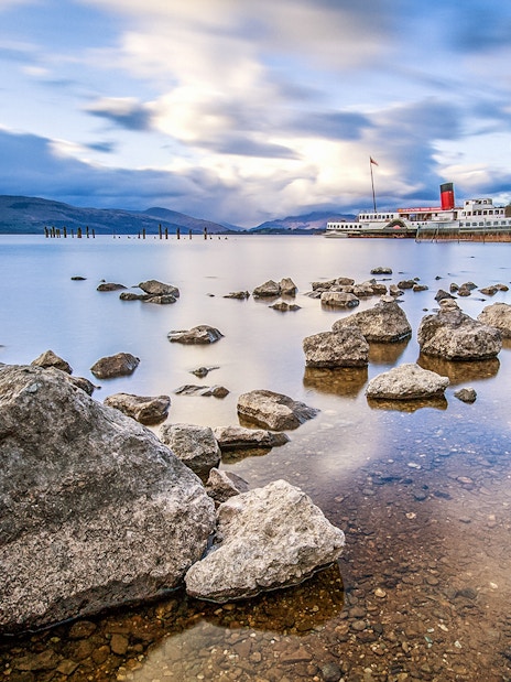 Steamboat on Loch Lomond Lake with rocky shoreline and distant hills.