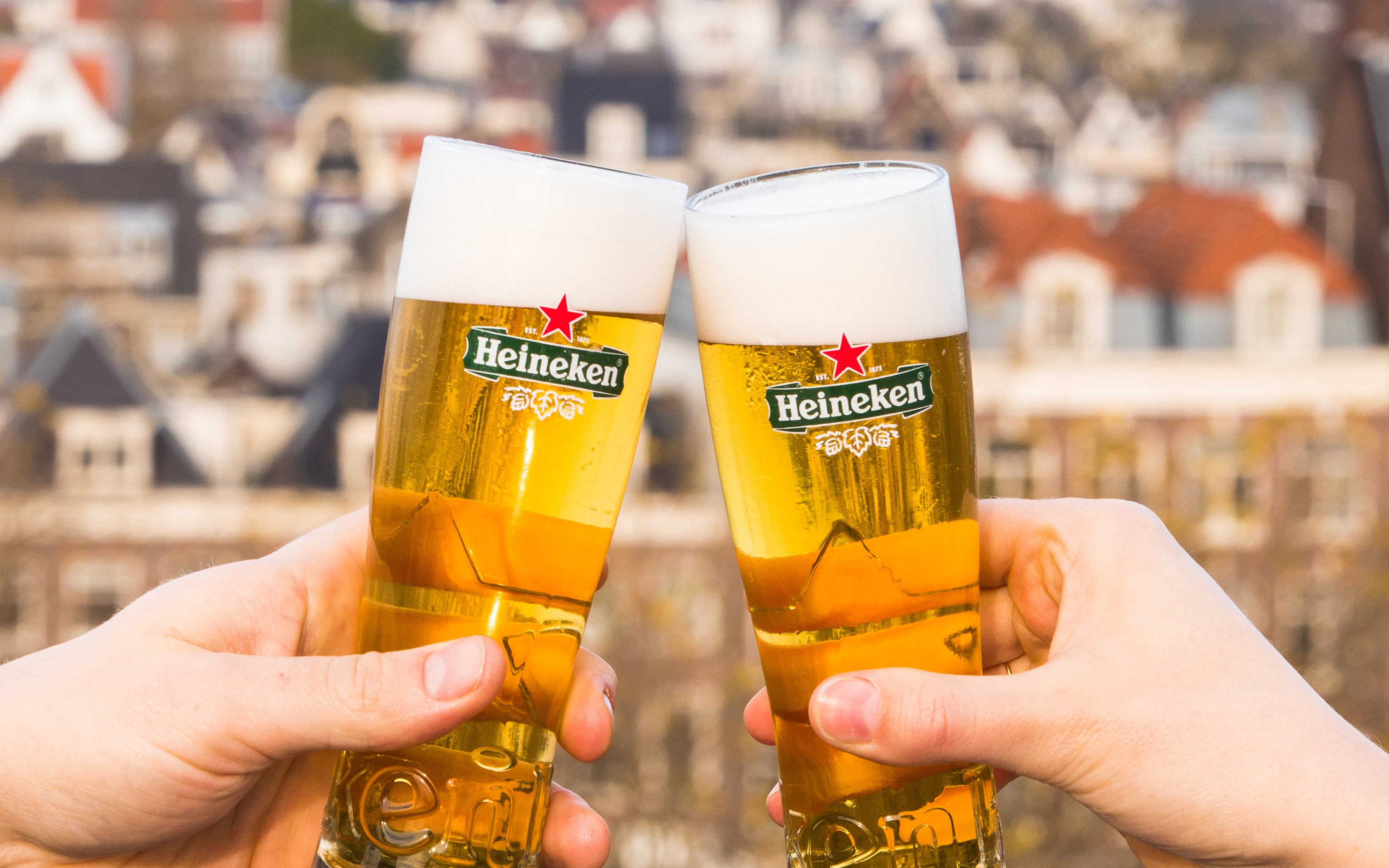 Cheers with Heineken beers on a rooftop with city view.
