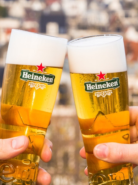 Cheers with Heineken beers on a rooftop with city view.