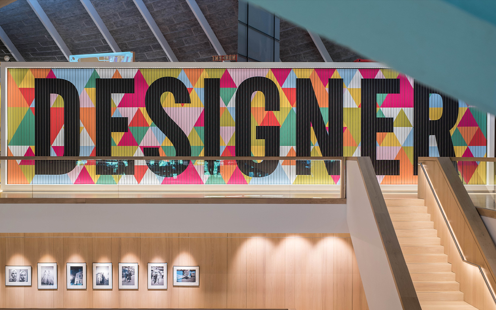 Colorful "Designer" sign inside London Design Museum with staircase and photo display.