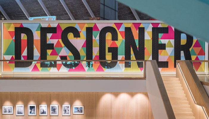 Colorful "Designer" sign inside London Design Museum with staircase and photo display.