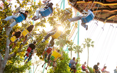 Visitors enjoying the swing ride at Knott's Berry Farm, surrounded by trees and sunlight.
