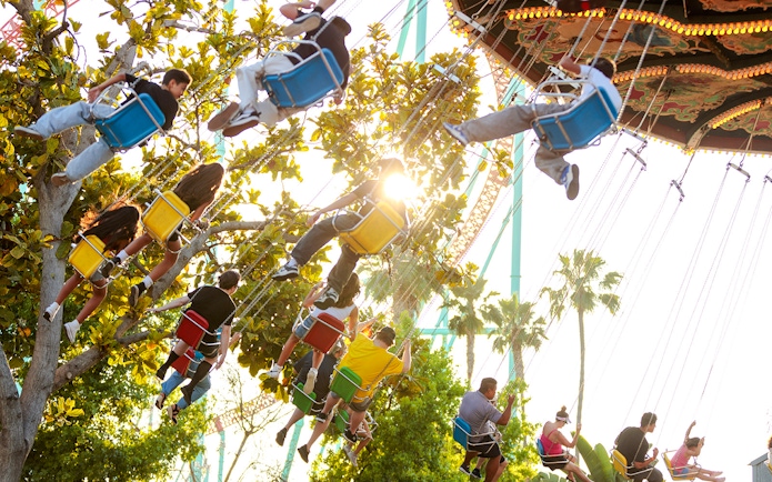 Visitors enjoying the swing ride at Knott's Berry Farm, surrounded by trees and sunlight.