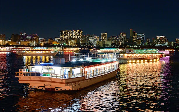Yakatabune boats illuminated on Tokyo Bay with city skyline in the background.