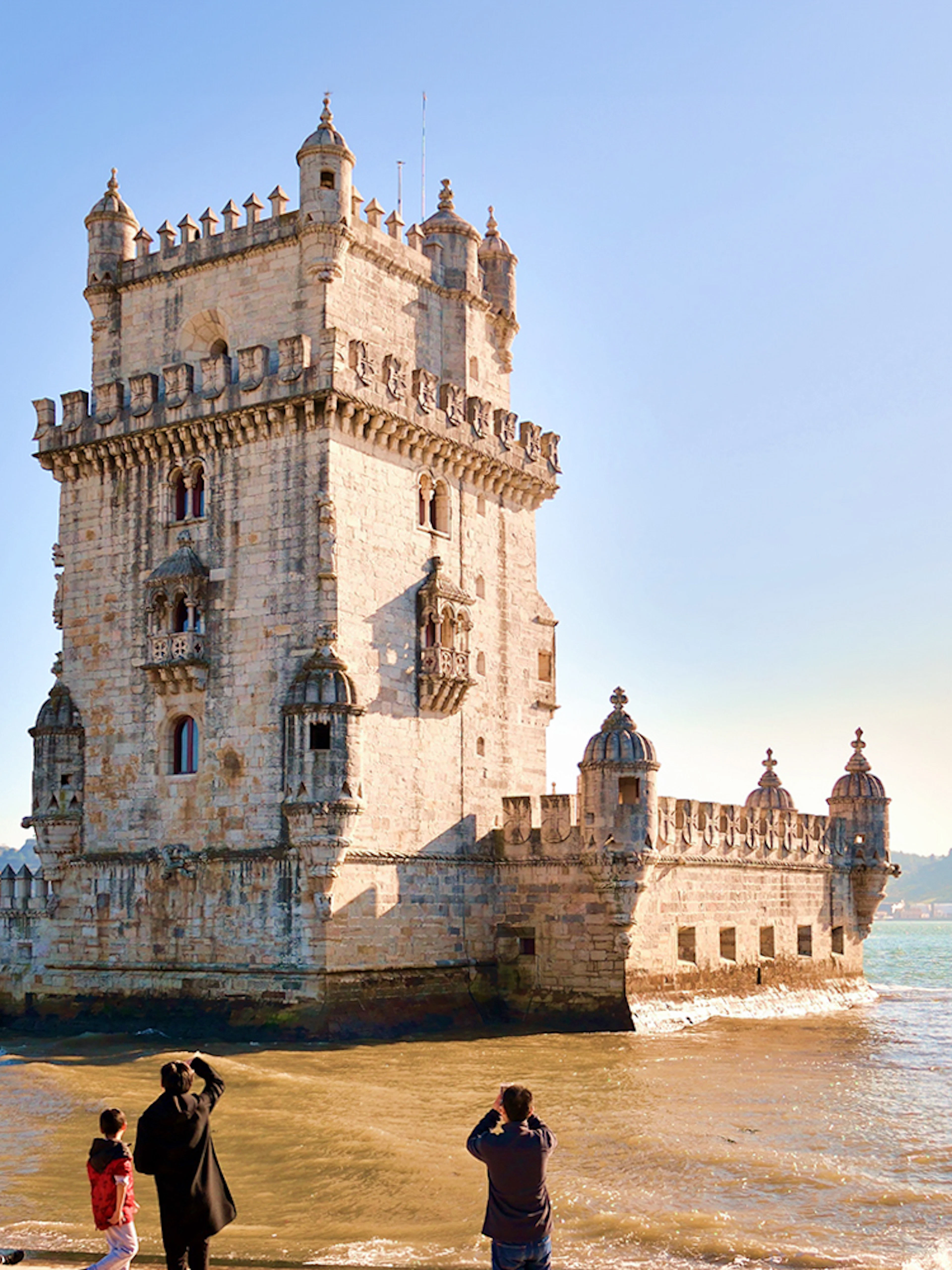 Tourists photographing Belem Tower by the Tagus River in Lisbon, Portugal.