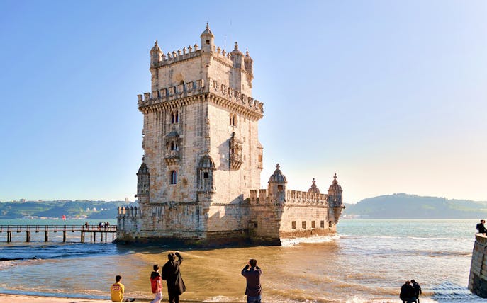 Tourists photographing Belem Tower by the Tagus River in Lisbon, Portugal.