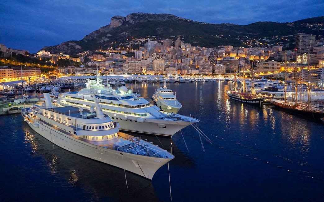 Monaco harbor at night with illuminated yachts and city skyline.