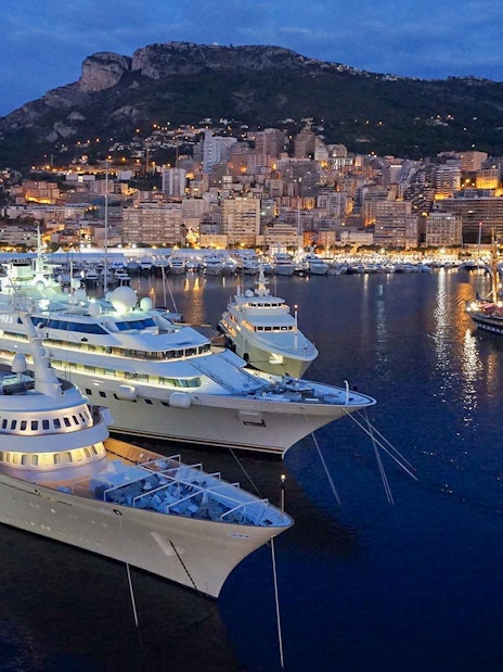 Monaco harbor at night with illuminated yachts and city skyline.