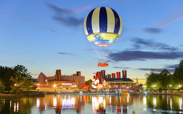 Ballon Panoramagique floating over a lit-up park at dusk in Paris, France.