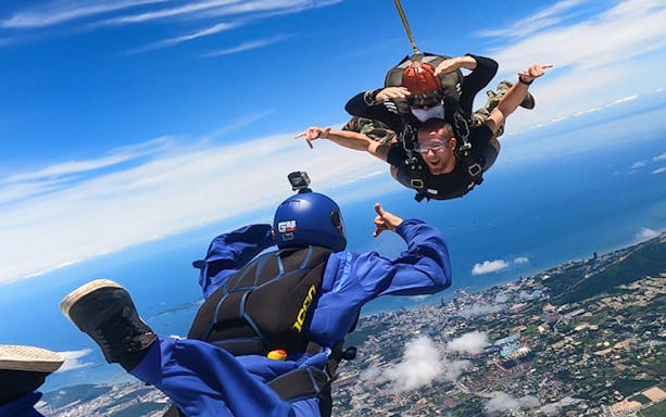 Skydiving instructor guiding a tandem jump over a coastal city.