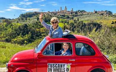 Vintage Fiat 500 driving through Tuscany with San Gimignano in the background.