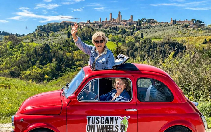Vintage Fiat 500 driving through Tuscany with San Gimignano in the background.