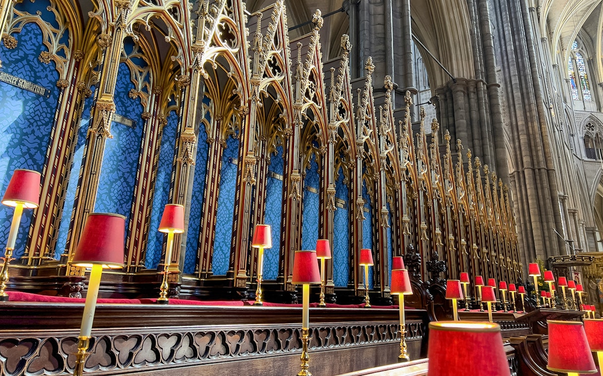 Westminster Abbey choir stalls with ornate gold detailing and red lamps.