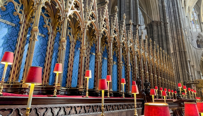 Westminster Abbey choir stalls with ornate gold detailing and red lamps.