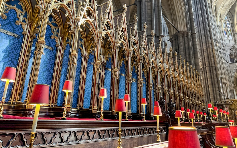 Westminster Abbey choir stalls with ornate gold detailing and red lamps.