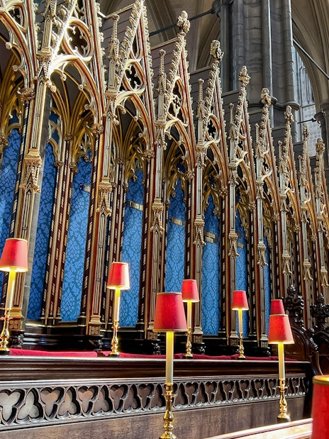 Westminster Abbey choir stalls with ornate gold detailing and red lamps.