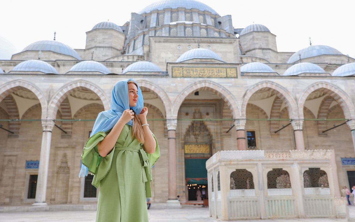 Visitor in courtyard of Blue Mosque, Istanbul, with domes and arches in the background.