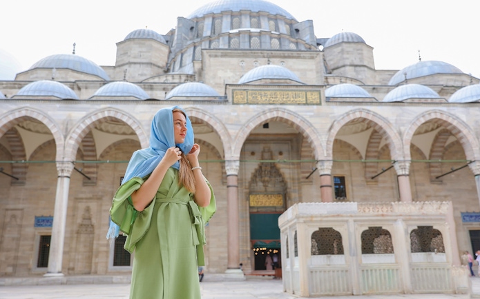 Visitor in courtyard of Blue Mosque, Istanbul, with domes and arches in the background.