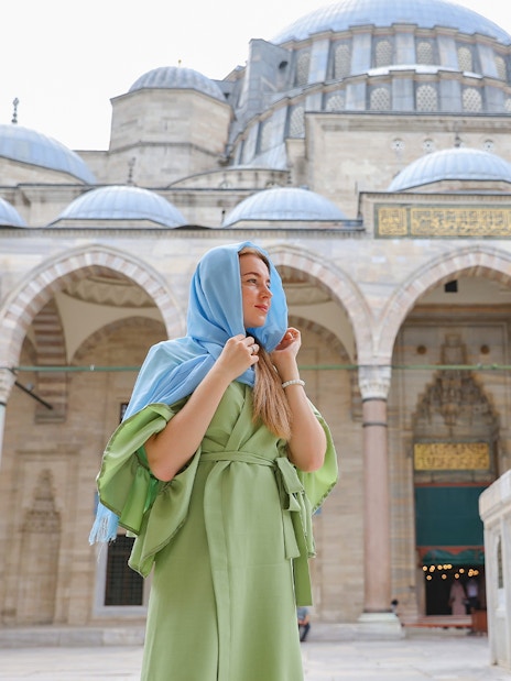 Visitor in courtyard of Blue Mosque, Istanbul, with domes and arches in the background.