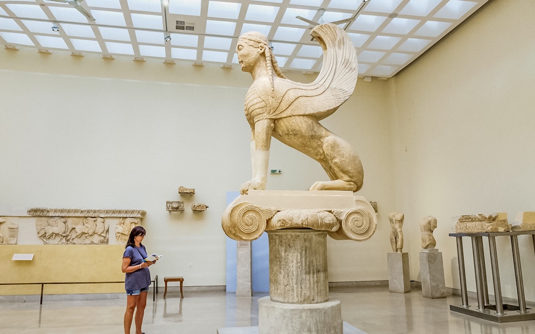 Tourist using audio guide near Sphinx statue in Delphi Museum, Greece.