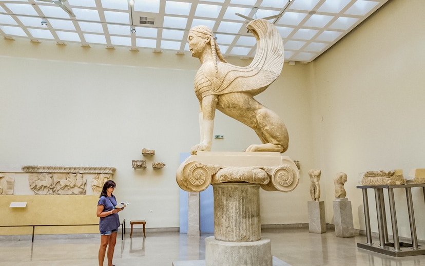 Tourist using audio guide near Sphinx statue in Delphi Museum, Greece.