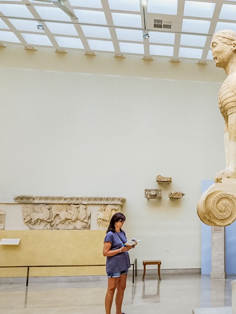Tourist using audio guide near Sphinx statue in Delphi Museum, Greece.